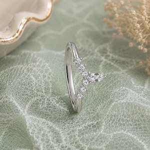 May include: A silver-toned V-shaped ring featuring a central marquise-cut clear stone flanked by three smaller round-cut clear stones on each side. The band is smooth and polished, creating a chevron silhouette that points outward from the finger.