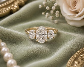 Peut inclure: Une bague en or avec une grande pierre centrale taille ovale entourée de deux pierres plus petites taille ronde. L'anneau est en or jaune poli et le sertissage maintient les trois pierres précieuses transparentes et facettées.