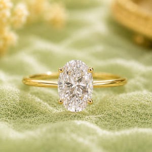 May include: A gold ring featuring a large, clear, oval-cut gemstone set in a four-prong mounting. The band is thin, polished, and circular, crafted from yellow gold. The centre stone is faceted, reflecting light with a brilliant, multi-faceted appearance.