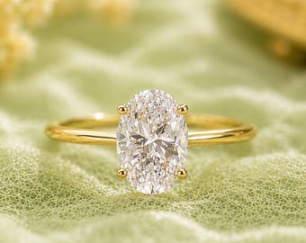 Peut inclure: Une bague en or avec une grande pierre précieuse transparente de taille ovale, fixée par quatre griffes. L'anneau est fin, poli et circulaire, fabriqué en or jaune. La pierre centrale est facettée, reflétant la lumière avec éclat.