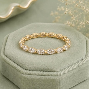 May include: A gold eternity band featuring a continuous row of marquise-cut clear stones set in a shared prong setting. The ring has a polished yellow gold finish and a delicate, slender profile, showcasing a repeating pattern of faceted gems.