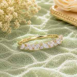 May include: A gold band ring featuring a series of marquise-cut and round-cut clear stones arranged in a delicate, repeating pattern along the top half of the band. The metal has a polished finish, and the stones are set securely in the gold setting.