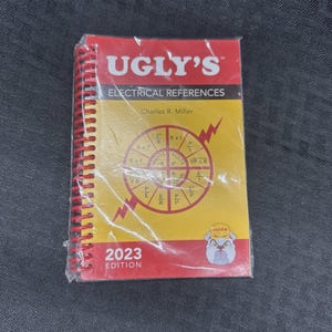 May include: A spiral-bound 2023 edition of Ugly's Electrical References book by Charles R. Miller. The cover is red and yellow with a central electrical formula wheel diagram, a bulldog mascot graphic, and clear plastic shrink-wrap packaging.