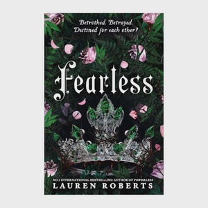 May include: A book cover titled Fearless by Lauren Roberts featuring a silver crown adorned with green gemstones. The background displays dark green foliage and pink rose petals. Text reads: Betrothed. Betrayed. Destined for each other? No.1 international bestselling author of Powerless.