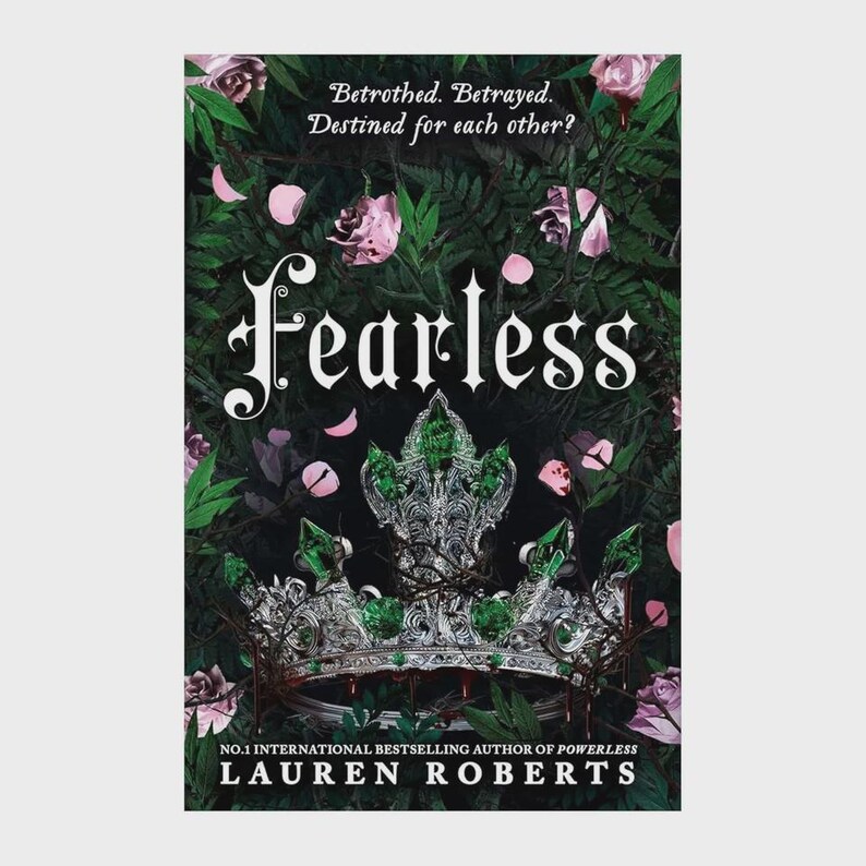 May include: A book cover titled Fearless by Lauren Roberts featuring a silver crown adorned with green gemstones. The background displays dark green foliage and pink rose petals. Text reads: Betrothed. Betrayed. Destined for each other? No.1 international bestselling author of Powerless.