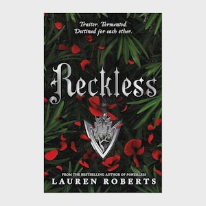 May include: The book cover for Reckless by Lauren Roberts features a silver arrowhead centred against a background of dark green foliage and scattered red petals. The title Reckless is printed in large silver lettering above the arrowhead.