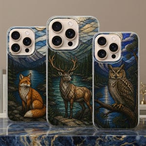 Puede incluir: Tres fundas para smartphone con ilustraciones de fauna en estilo vidriera. La funda izquierda muestra un zorro, la central un ciervo y la derecha un búho. Cada funda presenta un lago azul, un bosque y montañas de fondo.