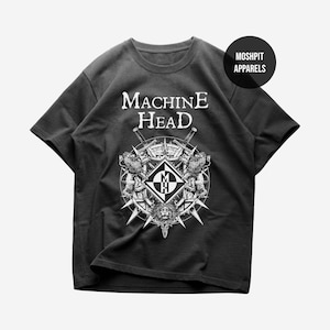 Puede incluir: Una camiseta gris carbón de manga corta con el texto blanco Machine Head sobre un gráfico circular con leones, espadas y un diamante central con las letras MH. Una insignia circular negra en la esquina superior derecha dice Moshpit Apparels.