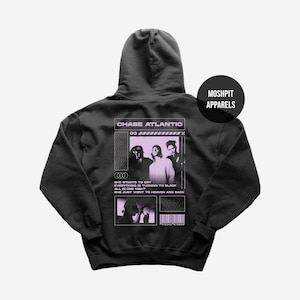 May include: A black hooded sweatshirt featuring a light purple graphic on the back. The design includes the text CHASE ATLANTIC, lyrics, a photograph of three people, and a barcode. A circular logo in the corner reads MOSHPIT APPARELS.