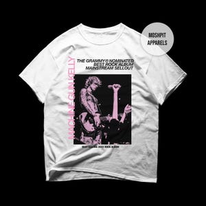 Könnte beinhalten: Weißes T-Shirt mit einer rosa-schwarzen Grafik von Machine Gun Kelly auf der Bühne. Der Text enthält "MACHINE GUN KELLY", "THE GRAMMY NOMINATED BEST ROCK ALBUM MAINSTREAM SELLOUT" und "BEST SELLING 2022 ROCK ALBUM". Das Shirt hat auch den Text "MOSHPIT APPARELS".