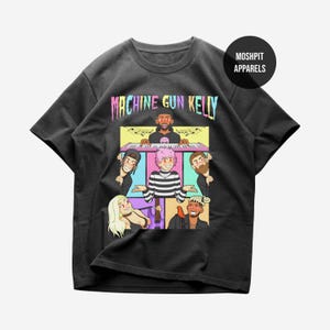 Könnte beinhalten: Schwarzes T-Shirt mit einer farbenfrohen Grafik mit dem Text "MACHINE GUN KELLY" und Cartoon-Illustrationen von Musikern. Das Shirt hat einen Rundhalsausschnitt und kurze Ärmel. Der Markenname "MOSHPIT APPARELS" ist ebenfalls sichtbar.