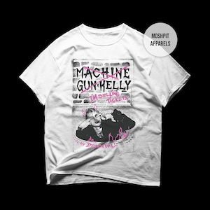 May include: White t-shirt featuring a graphic of Machine Gun Kelly with the text "MACHINE GUN KELLY I'M SELLING TICKETS" in pink and black. The design includes an image of the artist and flames.