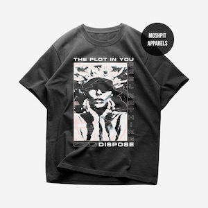 May include: A charcoal gray short-sleeve t-shirt featuring a graphic print of a person with a crown-like headpiece. The text reads THE PLOT IN YOU, FEEL NOTHING, and DISPOSE. A circular logo in the top right corner displays MOSHPIT APPARELS.