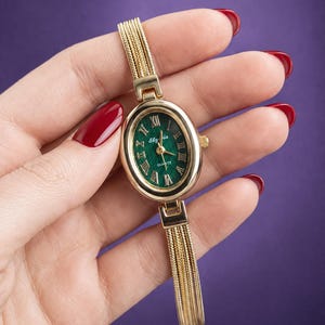 May include: An oval-shaped gold-tone watch with a deep green textured dial. The watch face features gold Roman numeral hour markers, gold hands, and the text "Slyria" and "Quartz" printed in white. It has a multi-strand gold-tone chain bracelet.