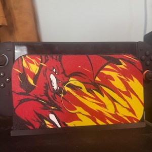 May include: A black video game console dock featuring a custom front plate with a graphic illustration of a red dragon breathing yellow and orange flames. The dragon is depicted in a dynamic pose with black outlines against a vibrant red background.