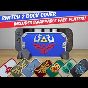 Può includere: Una cover per dock di console da gioco con una piastra frontale blu e un emblema dorato e rosso. Il set include diverse piastre frontali intercambiabili con vari design colorati. Il testo recita: SWITCH 2 DOCK COVER INCLUDES SWAPPABLE FACE PLATES!!