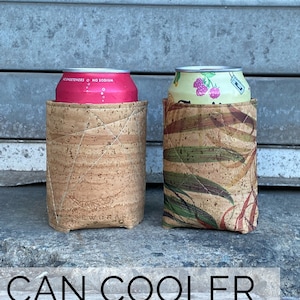 May include: Two cork-lined beverage koozies, one with a pink can and the other with a green and brown can. The koozies are made with self-healing edge textiles and are a great beginner sewing project. The text "CAN COOLER LINED BEVERAGE KOOZIE" is at the bottom of the image.