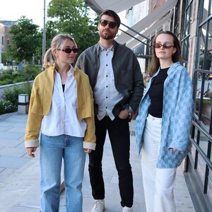Pode incluir: Tr&ecirc;s pessoas vestindo roupas casuais. A pessoa &agrave; esquerda usa uma jaqueta curta amarelo-mostarda, camisa branca e cal&ccedil;a jeans azul. A pessoa ao centro usa jaqueta cinza-escura, camisa branca e cal&ccedil;a preta. A pessoa &agrave; direita usa jaqueta xadrez azul-clara, blusa preta e cal&ccedil;a branca.