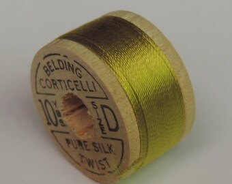 May include: A spool of Belding Corticelli pure silk twist thread, size D, in a vibrant yellow-green color. The wooden spool has printed text and is partially visible. The thread is tightly wound around the spool.