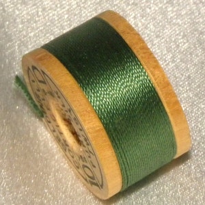 May include: A spool of dark green thread wound around a wooden bobbin. The bobbin is labeled "DMC 101".