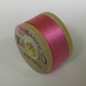 May include: A wooden spool of pink silk twist thread labeled "Elegance Silk Twist 10 yds."
