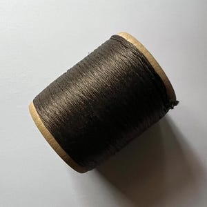 May include: A spool of dark brown thread wound around a cardboard bobbin.