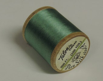 May include: A spool of green Talon Pure Silk thread. The wooden spool has a label with the text "Talon Thread" and "300 ft. (100 YDS.)". The thread is a solid, muted green color.