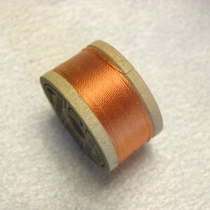 May include: A spool of orange thread wound around a wooden bobbin.