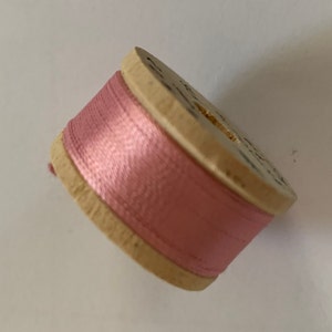 May include: A spool of pink thread wound around a wooden bobbin.