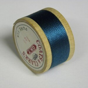 May include: A spool of dark blue Coats & Clark's thread labeled "ON'T 140 PURE SILK" on a wooden bobbin.