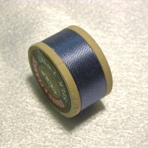 May include: A spool of blue silk thread with a label that reads "COATS'S SIX CORD SILK 120 YARDS".