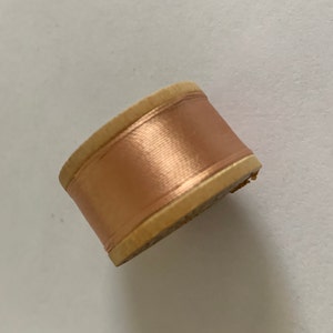 May include: A spool of copper wire wrapped around a wooden bobbin. The wire is a shiny, metallic copper color.