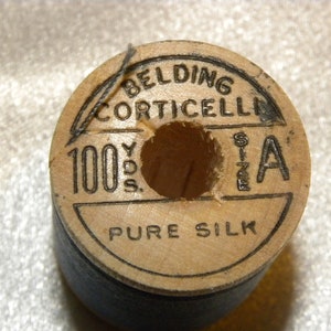K&ouml;nnte beinhalten: Eine Holzspule mit schwarzem Garn mit der Aufschrift "Belding Corticelli 100 Yds. Size A Pure Silk"