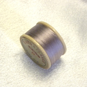 May include: A spool of Coats & Clark's Pure Silk thread in a light purple color. The spool is labeled "Coats & Clark's Pure Silk".