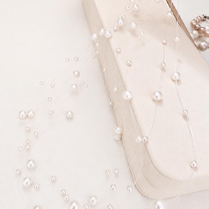 May include: A multi-strand necklace featuring numerous white, round, lustrous pearls of varying sizes suspended on thin, clear, transparent nylon fishing line, creating a floating effect across the multiple delicate strands of the jewelry piece.