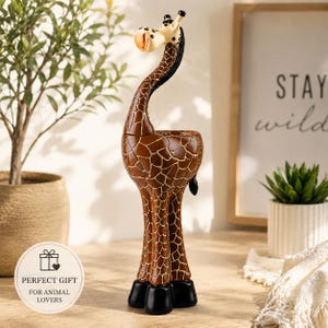 May include: A tall giraffe figurine featuring a brown body with a white grid pattern, a long neck, and black hooves. The giraffe has a cream-colored head with dark spots and a small black mane. The sculpture stands upright on a flat surface.