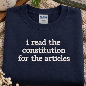 May include: A navy blue crewneck sweatshirt featuring white embroidered text that reads "i read the constitution for the articles" centered on the chest. The garment includes a Gildan brand label at the inner neckline indicating a size large.