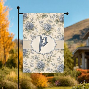 May include: A rectangular garden flag featuring a cream-colored background with a repeating pattern of blue hydrangea flowers and green foliage. A horizontal band across the center contains a decorative frame with the capital letter P in blue.