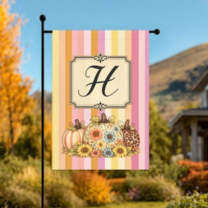 May include: A rectangular garden flag featuring vertical stripes in shades of pink, orange, and yellow. A central cream-colored rectangular frame contains a large black letter H. Below, three pumpkins are decorated with floral and leopard patterns.