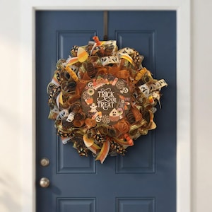 Può includere: Una ghirlanda di Halloween realizzata con nastri a rete arancioni, neri e bianchi con un cartello circolare centrale che riporta la scritta Trick or Treat, circondata da illustrazioni di fantasmi, caramelle e dolciumi su sfondo marrone.