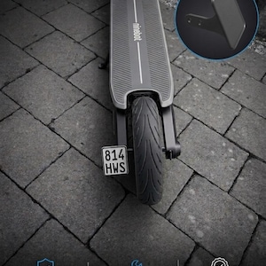 May include: A black Ninebot electric scooter deck with a textured surface and a rear tyre. A number plate holder with the text 814 HWS is attached to the rear. An inset circle shows a black metal number plate mounting bracket with two holes.