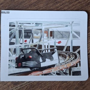 May include: A rectangular sticker featuring a detailed illustration of a black and white cow-patterned roller coaster car on a metal track. The background shows a white structural framework with two small red mouse silhouettes. The text 669200 is visible.