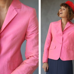 May include: A pink blazer with a single button closure and two pockets. The blazer is made of a lightweight fabric and has a relaxed fit.