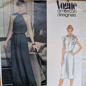 May include: Vintage Vogue American Designers sewing pattern featuring two dress designs. One dress is a dark, halter-style gown with a sheer, dotted cape. The other is a white, knee-length dress with a bow detail at the neckline. The pattern is by Edith Head.