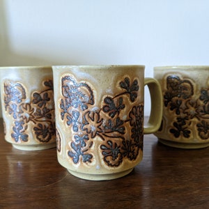May include: Three ceramic mugs with a brown and beige floral pattern. The mugs have a rounded shape and a handle.