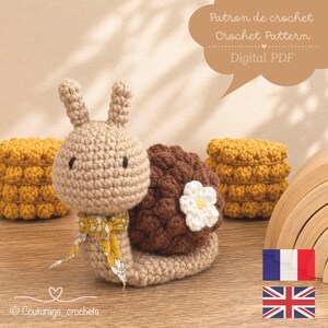 Peut inclure: Un escargot en crochet beige avec une coquille texturée marron foncé, une petite fleur blanche et un ruban jaune à motifs floraux. Une bulle en haut contient le texte : Patron de crochet, Crochet Pattern, Digital PDF.