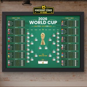 May include: A framed 2026 World Cup match schedule poster with a green background, featuring a gold trophy illustration in the centre, group stage listings with national flags, and a knockout stage bracket. The text reads Knockout Stage Is Here.