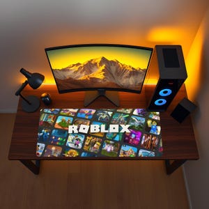 以下が含まれることがあります： 様々なRobloxゲームシーンのコラージュと、表面中央に白いRobloxロゴが配置された長方形のデスクマット。このマットは、湾曲したコンピューターモニターとデスクトップタワーコンピューターの前のダークウッドのデスクの上に置かれています。