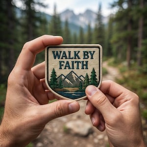 May include: A shield-shaped embroidered patch featuring the text WALK BY FAITH in dark green letters. The design includes a landscape with a blue lake, green pine trees, and grey mountains against a cream-colored background with a dark border.