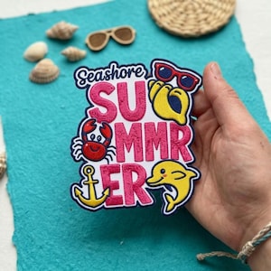 May include: An embroidered patch featuring the text Seashore SUMMER in pink letters. The design includes a red crab, a yellow anchor, a yellow dolphin, and a pair of red sunglasses. The patch has a dark blue border and a white background.